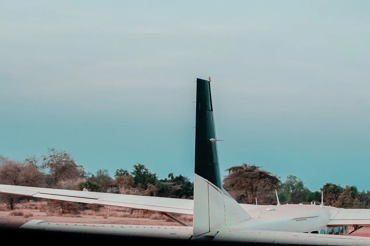 A light aircraft with a dark green tail parked on a red-brown airstrip in Nyerere National Park under a teal sky